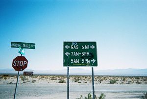 road sign, altered by graffiti, advising where and when gasoline can be obtained nearby